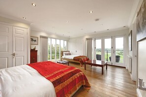 A spacious bedroom with a large bed, a second smaller bed, a wooden table, and a view of the outdoors through large sliding doors.