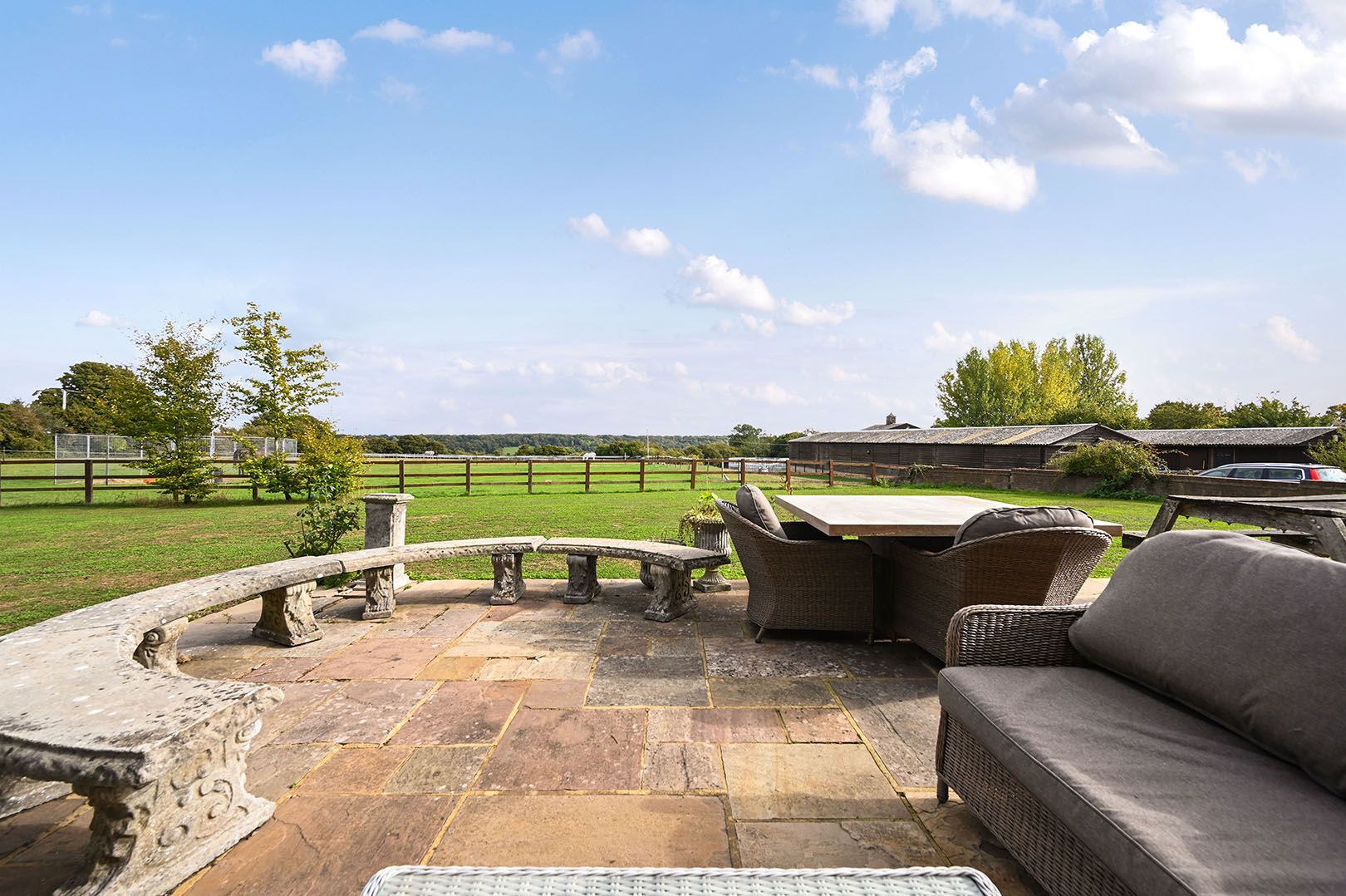 Een terras buiten met stenen vloeren, rieten meubels en uitzicht op een landelijk landschap.