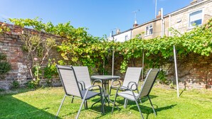 A patio with a table and four chairs, surrounded by a brick wall and greenery. - Comfy, 2 Bed House, Sleeps 6 with Garden and Free Parking in Cheltenham (Cheltenham)