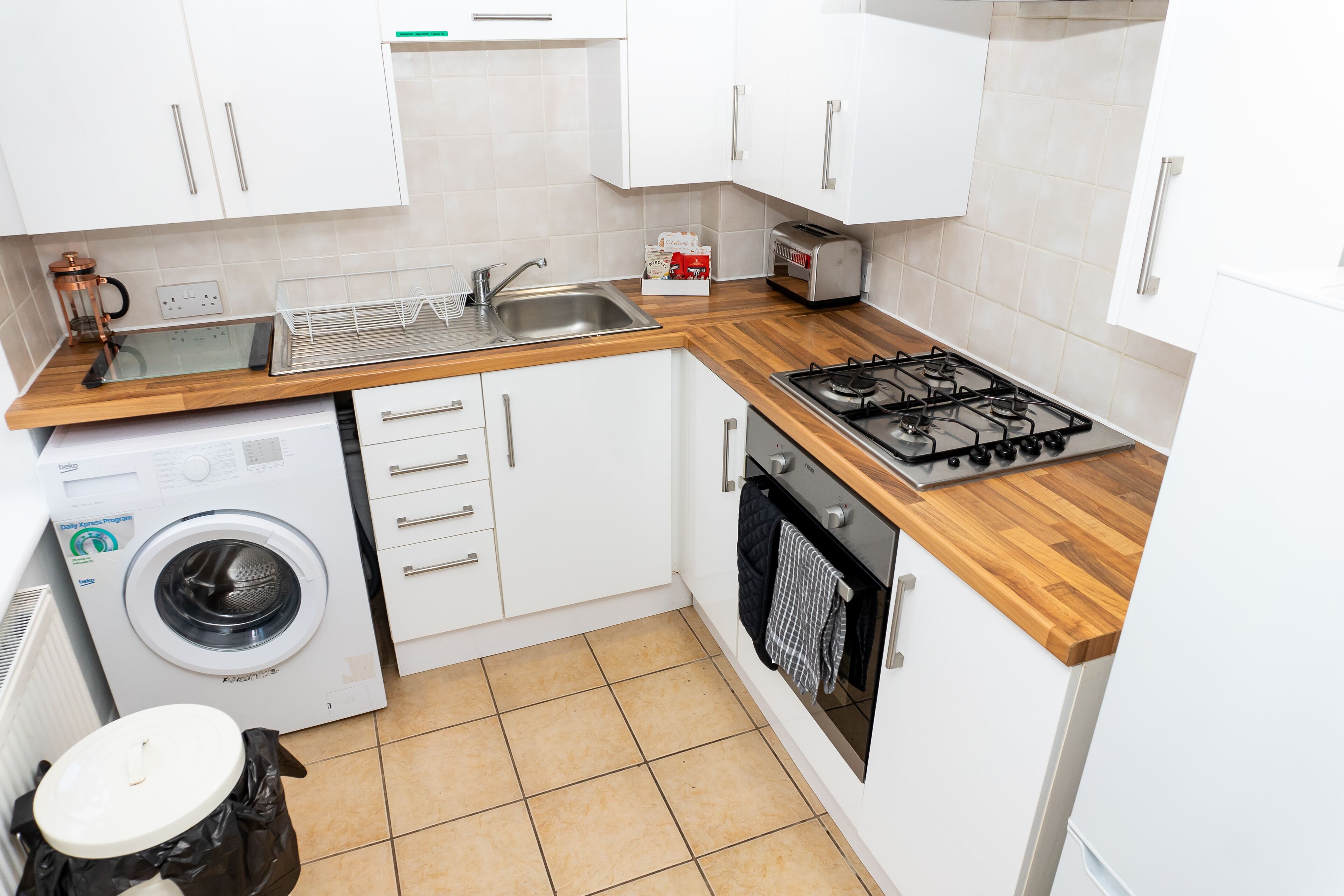 Une cuisine de taille réduite avec des meubles blancs, un lave-linge, une cuisinière et un évier.