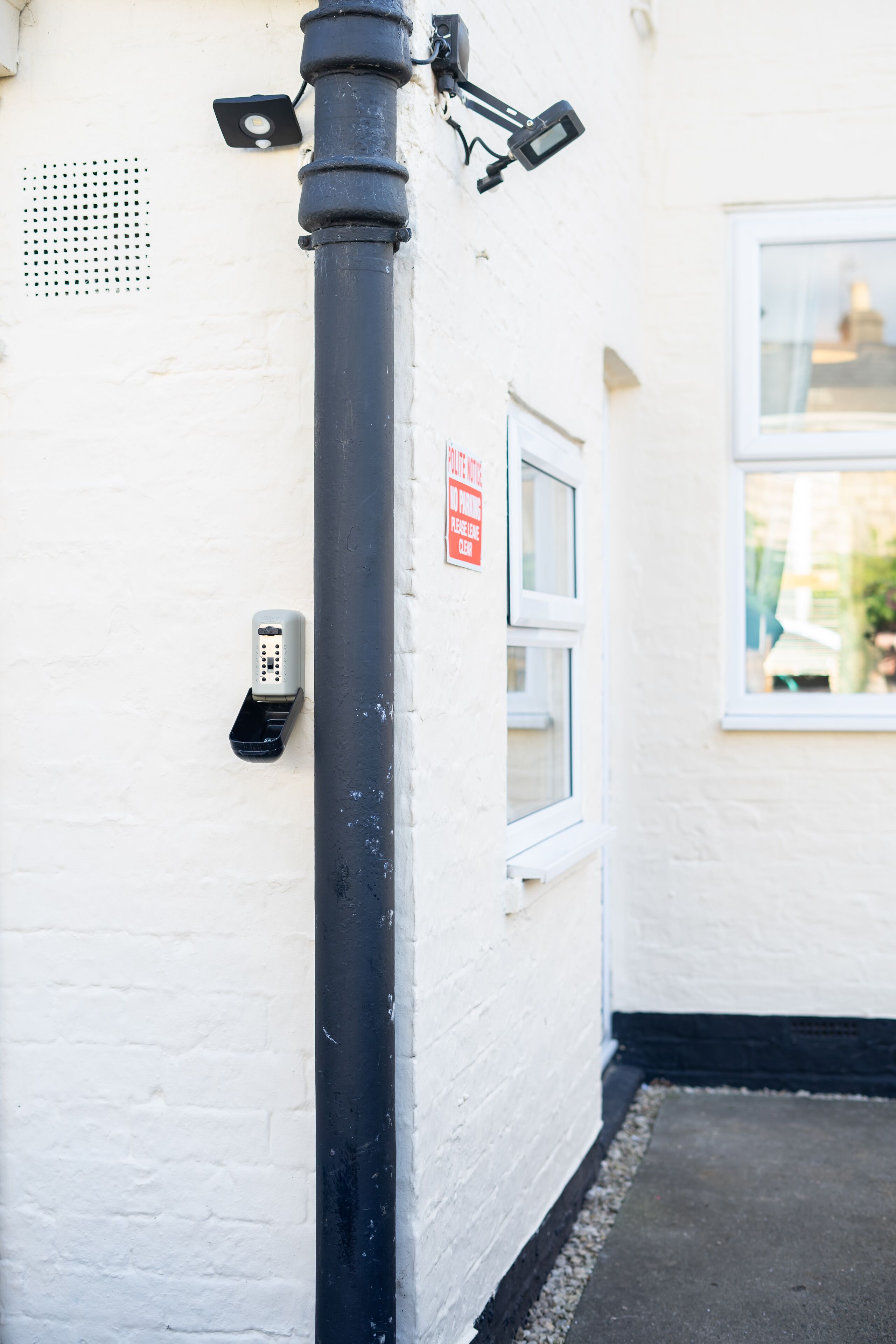 A black pole with a security camera and a parking meter on a white wall.