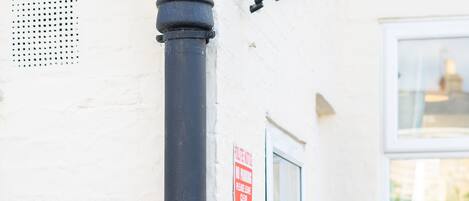 A black pole with a security camera and a parking meter on a white wall.