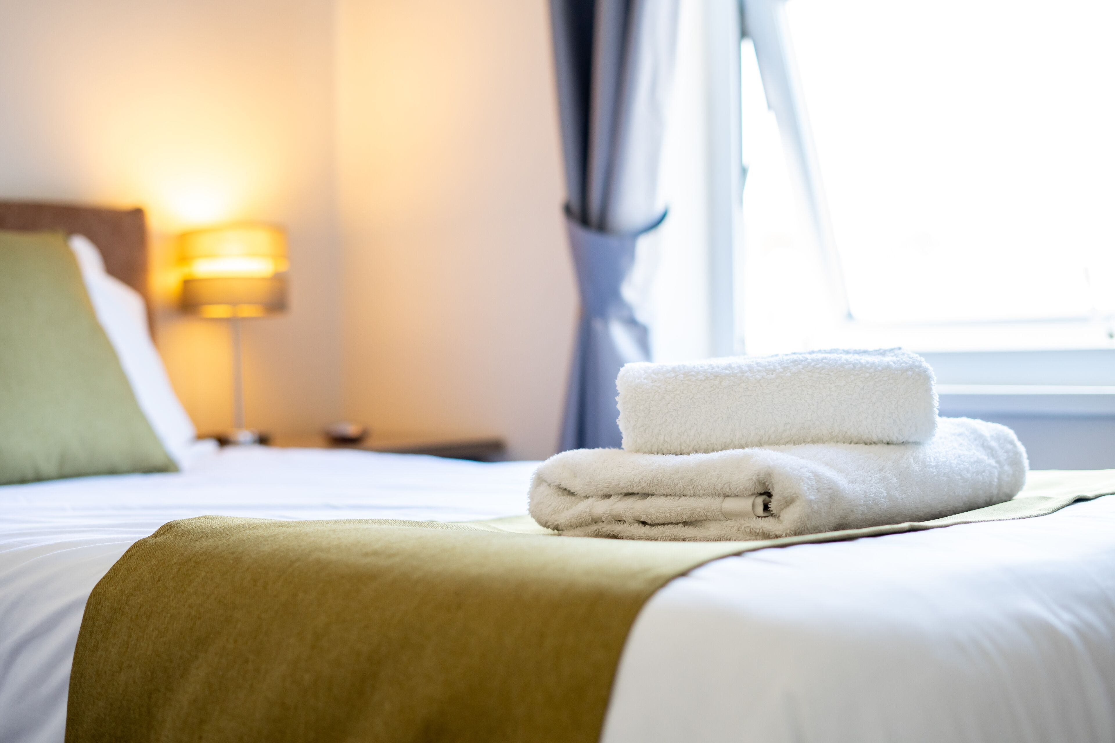 A neatly made bed with a folded white towel and a beige throw blanket.
