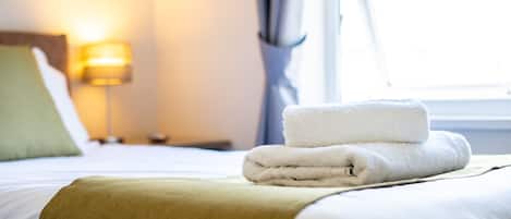 Una cama bien hecha con una toalla blanca doblada y una manta beige.