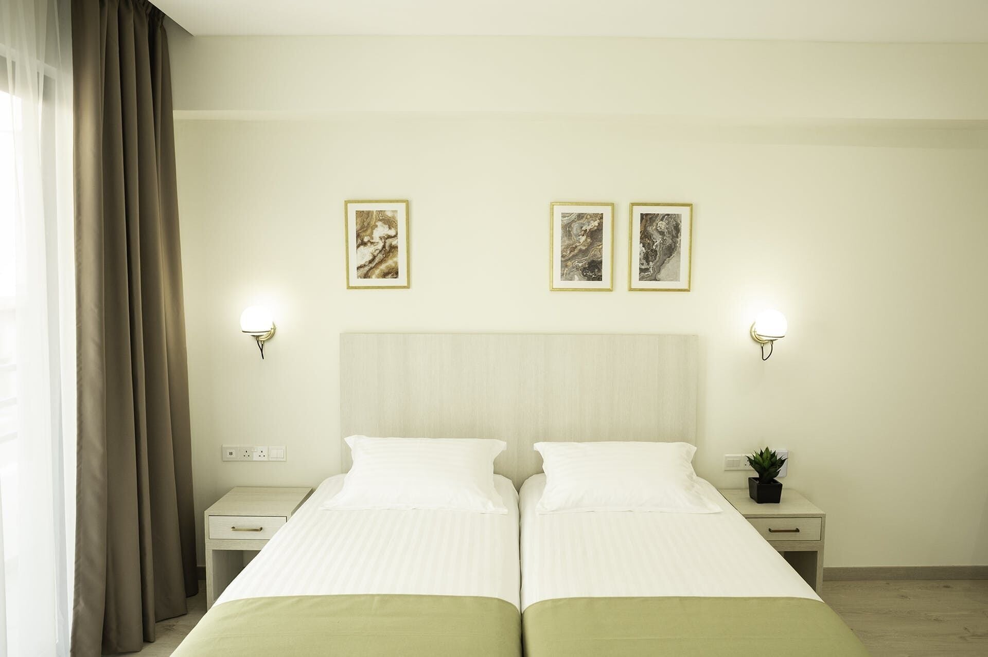 A double bed with a light-colored headboard, two bedside tables with lamps, and two framed pictures on the wall.