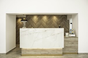 Un mostrador de recepción con encimera de mármol, pared revestida de madera y una lámpara a la izquierda.