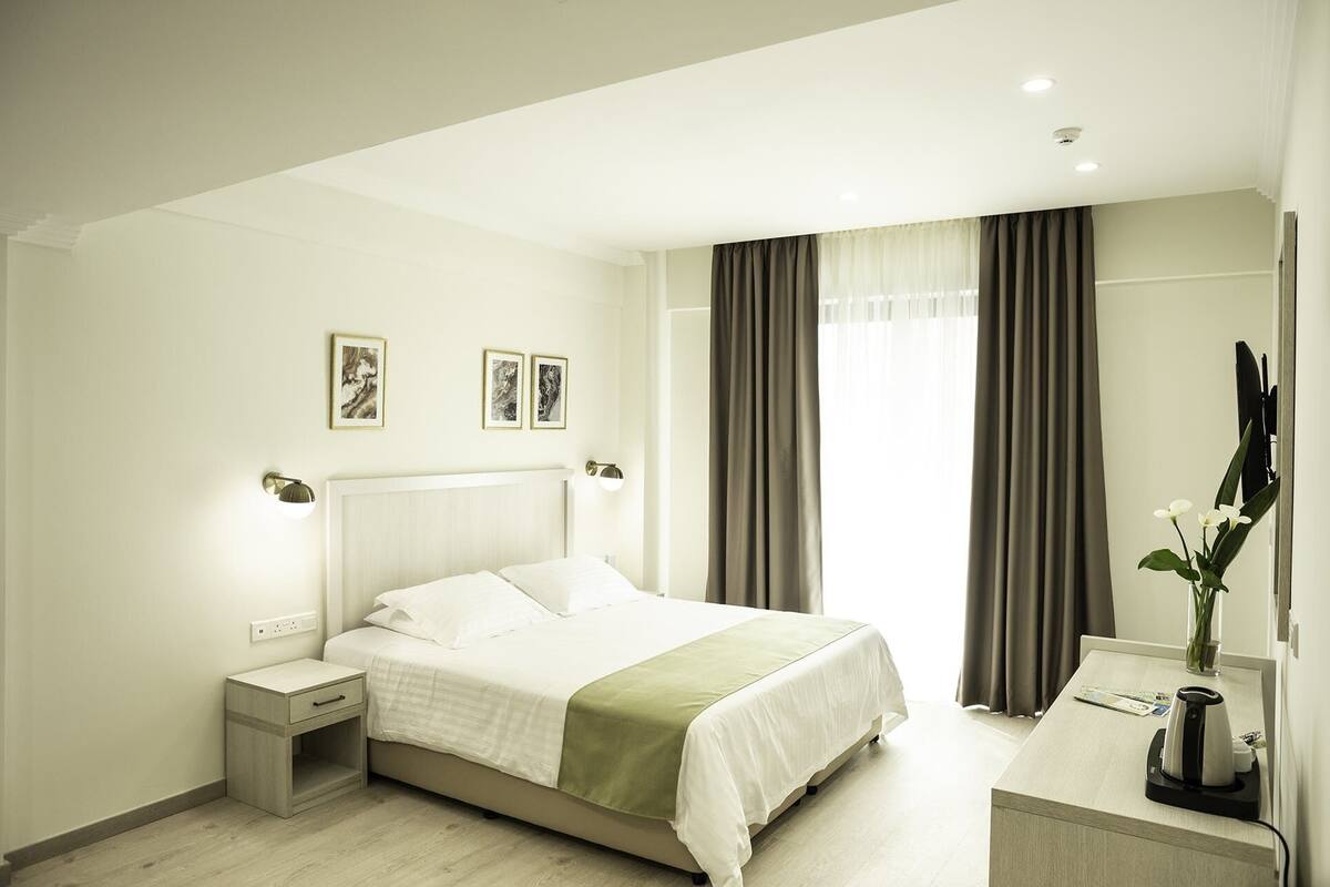 A modern hotel room with a large bed, bedside tables, a desk, and a mirror.