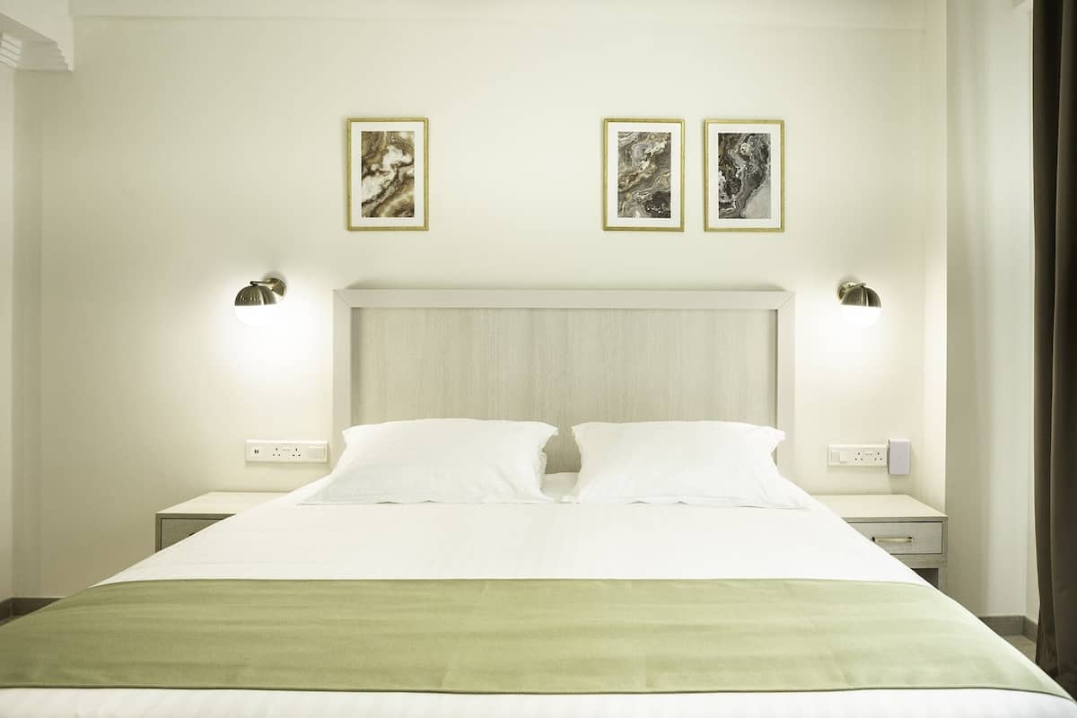 A hotel room with a large bed, two bedside tables, and two wall-mounted lamps.
