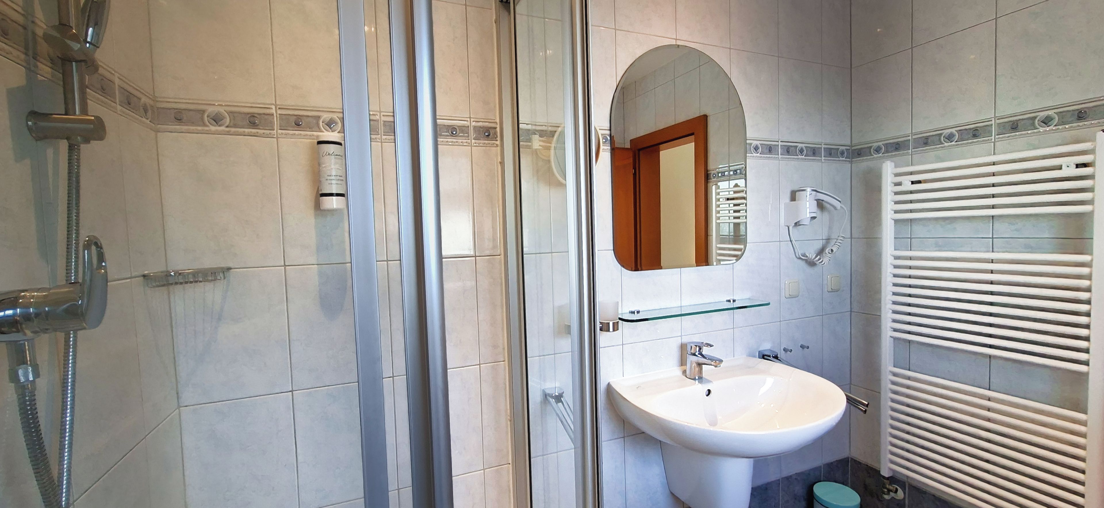 Un baño con cabina de ducha de vidrio, un lavamanos blanco y un perchero para toallas.