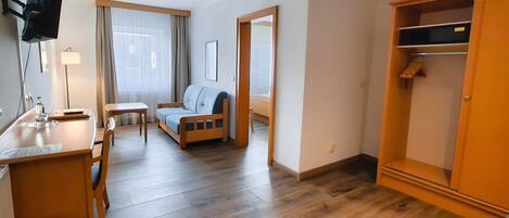 Ein Hotelzimmer mit Bett, Schreibtisch, Stuhl, einem kleinen Tisch, einem Kleiderschrank und einem Fernseher.