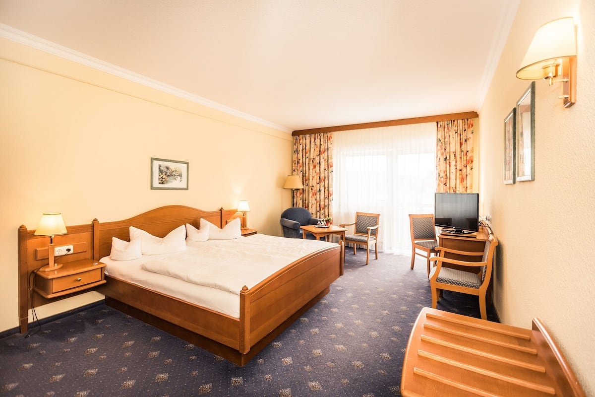 Hotellihuone, jossa on suuri sänky, työpöytä tuolilla, televisio ja pieni pöytä lampun kanssa.