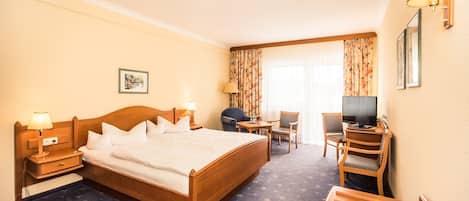 Habitación de hotel con una cama grande, un escritorio con silla, televisión y una mesita con lámpara.
