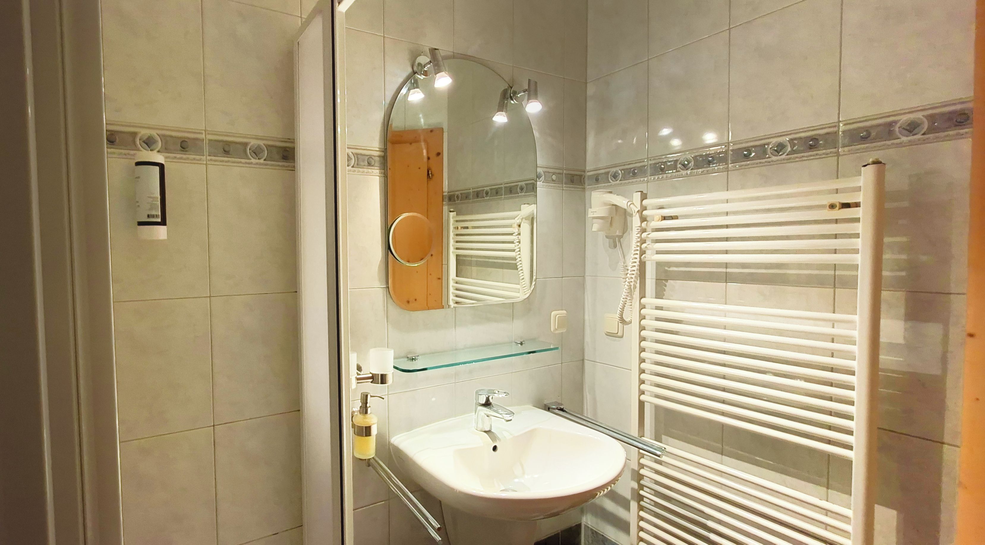 Un baño con cabina de ducha de vidrio, un lavamanos blanco con repisa de vidrio y un perchero con toallas blancas.