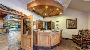 A wooden reception desk with a glass partition, a wooden ceiling with recessed lighting, a patterned sofa, and a framed picture on the wall. - Hotel Nordkap (Karlshagen)