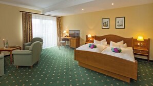 A hotel room with a large bed, two bedside tables with lamps, a desk with a computer, a chair, and a window with curtains. - Hotel Nordkap (Karlshagen)