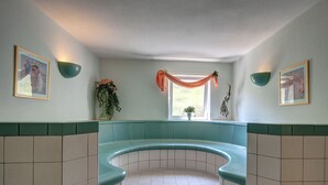 A curved bench seating area with a tiled floor, framed pictures on the walls, and a window with a draped curtain. - Hotel Nordkap (Karlshagen)