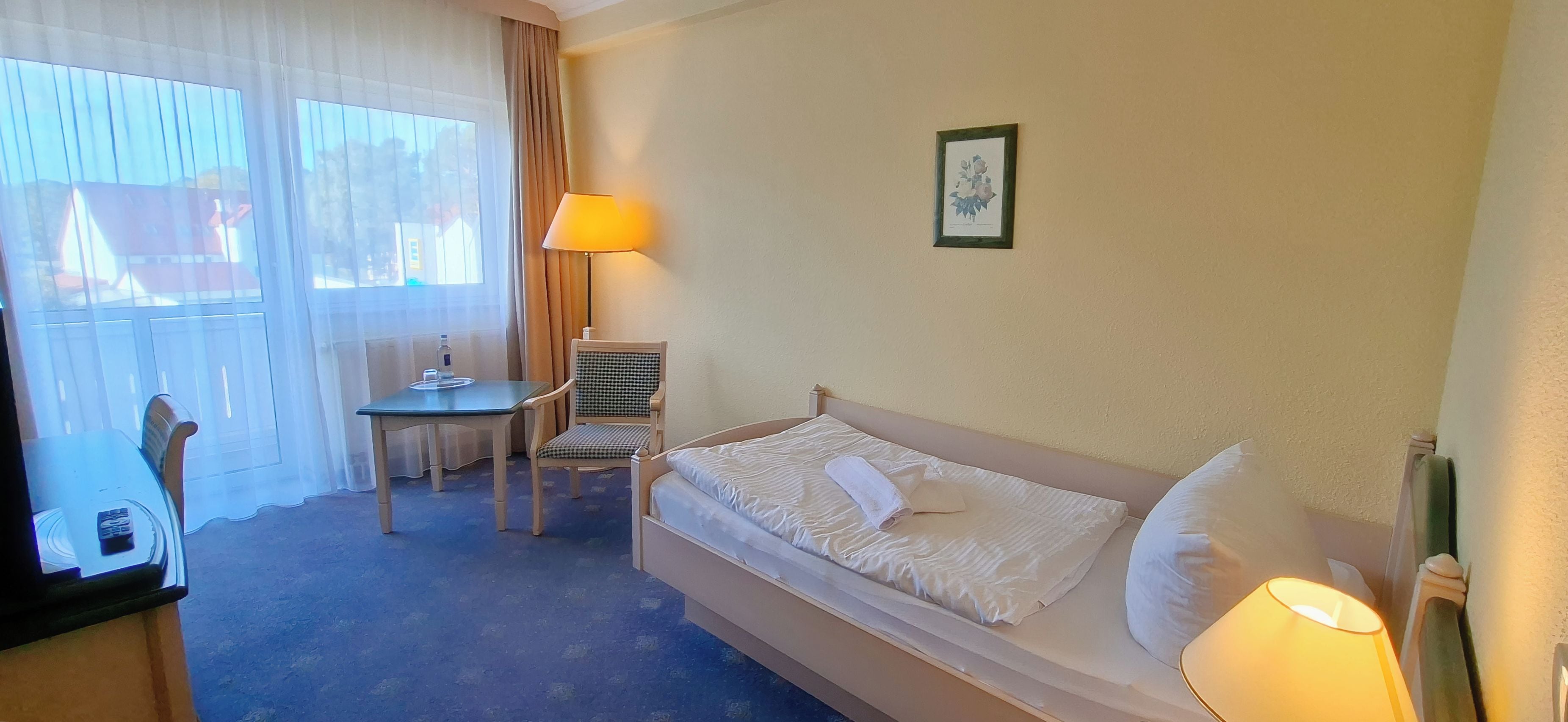 Una habitación de hotel con una cama, una silla, una mesa y una lámpara.
