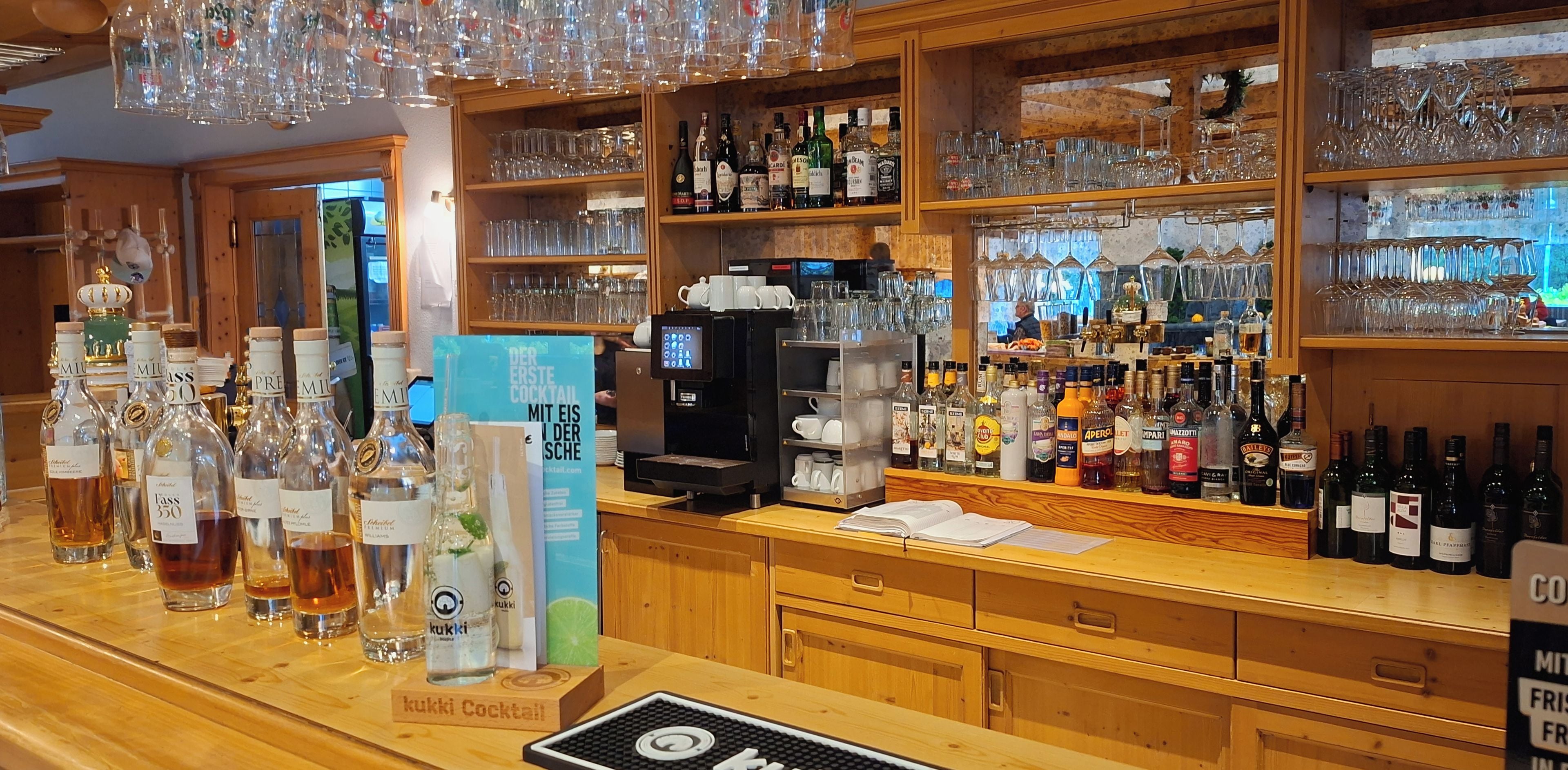 A bar area with shelves of liquor bottles, glasses, and a coffee machine.