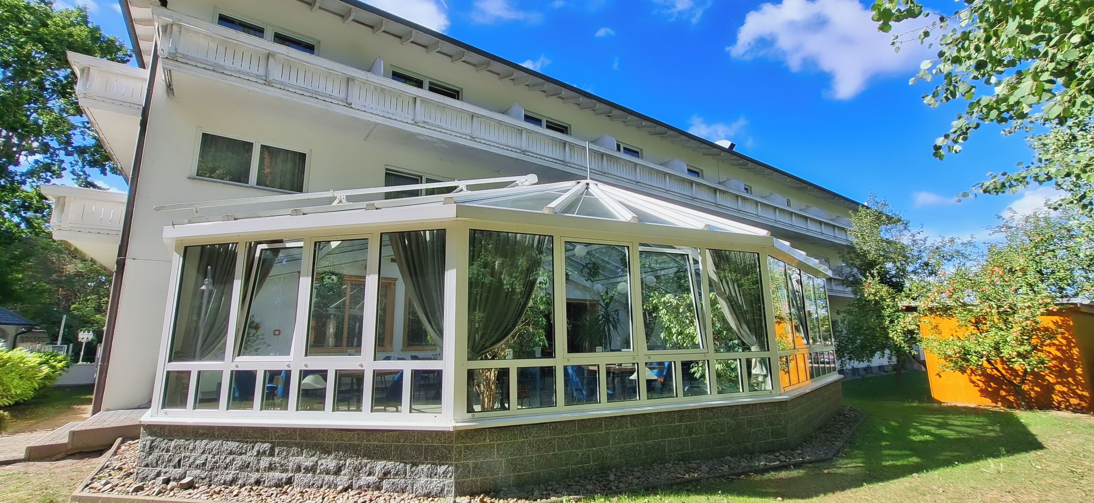 A two-story building with a conservatory featuring multiple glass panes and a white frame.