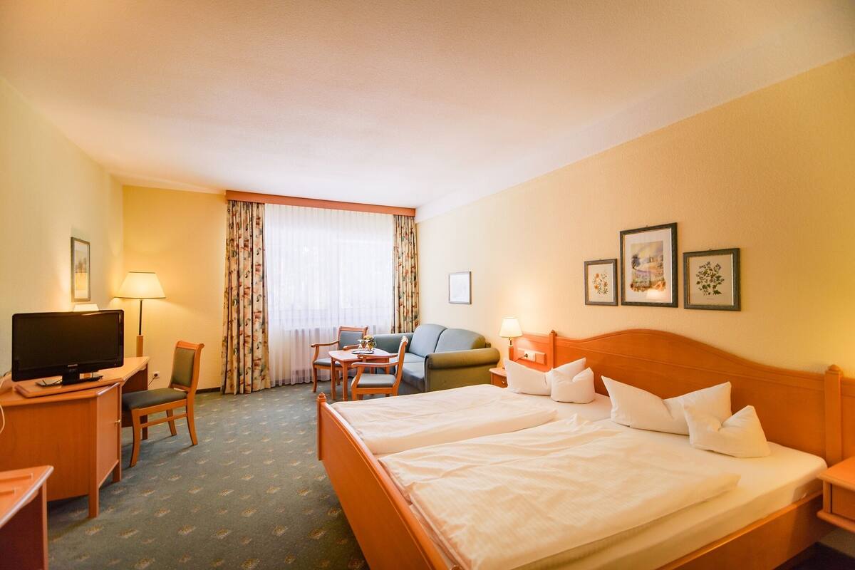Hotellihuone, jossa on sänky, työpöytä tietokoneella, tuoli, sohva ja televisio.