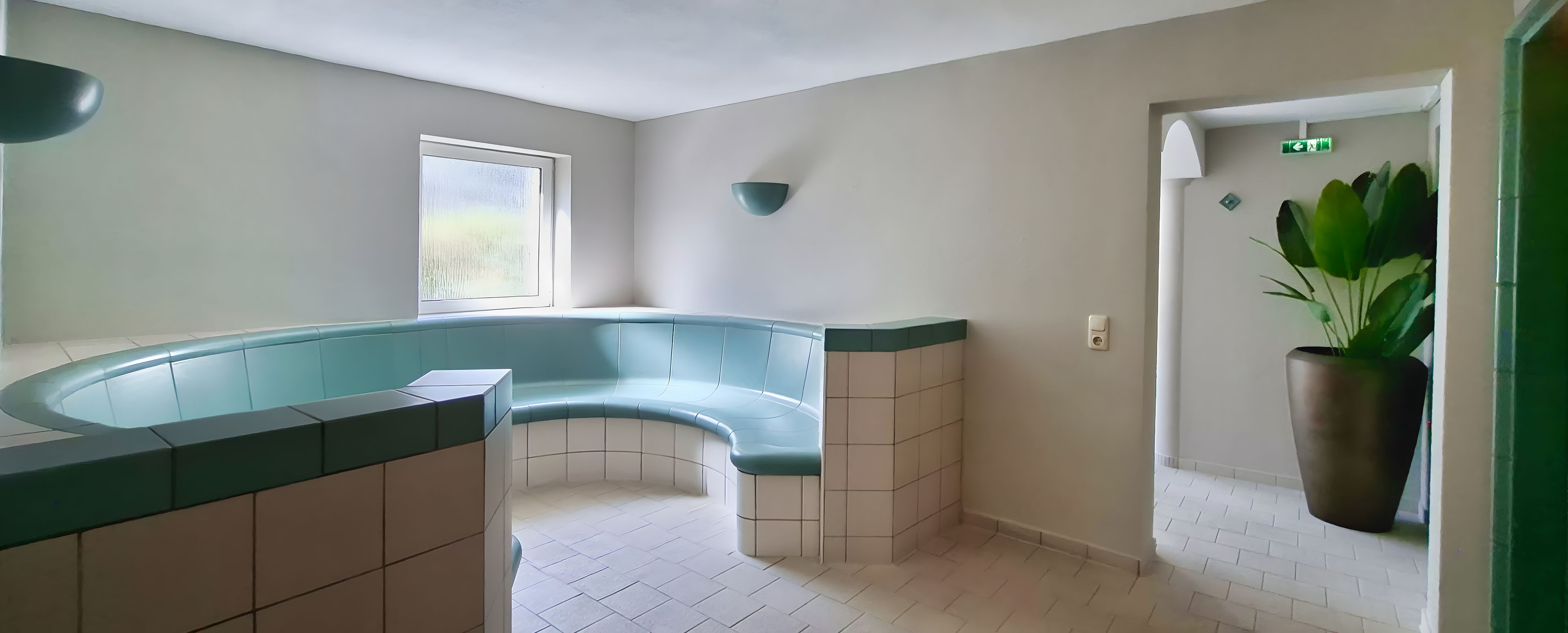 Un espace de détente avec un coin salon aux lignes courbes, une fenêtre et une plante en pot.
