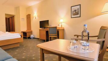 A hotel room with a bed, a desk, a chair, a TV, a lamp, and a table with a bottle and glasses.