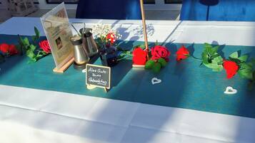 Una mesa con mantel azul, rosas rojas, un letrero pequeño y una cafetera.
