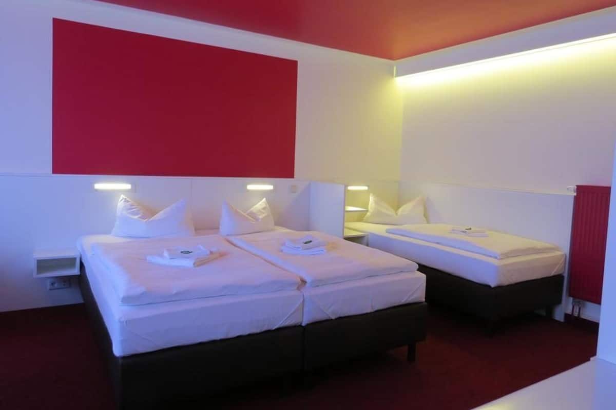 A hotel room with two beds, white bedding, and red accents on the walls.