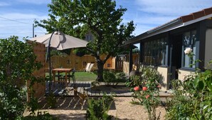A backyard with a wooden deck, a table with chairs, a covered seating area, and a garden with roses. - Spacious and bright family accommodation in Chazelles-sur-Lyon (Chazelles-sur-Lyon)