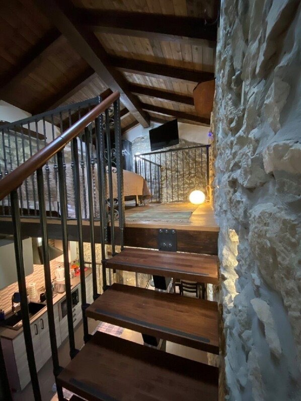 A rustic staircase with wooden steps and metal railings, leading to a stone wall with a warm light source.