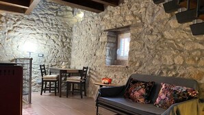 A cozy room with a stone wall, a sofa with patterned cushions, a dining table with chairs, and a small window. - Ancient turret of 1800 surrounded by nature - whole structure (Barbarolo)