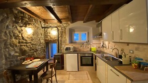 A compact kitchen with a stone wall, wooden ceiling beams, a dining table with chairs, and basic appliances. - Ancient turret of 1800 surrounded by nature - whole structure (Barbarolo)