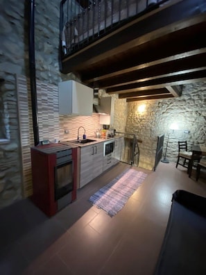 A kitchen with a stone wall, wooden beams, and a dining area with a table and chairs.