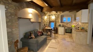 A cozy interior with a stone wall, a wooden ceiling, a sofa, a dining table, and a kitchen area. - Ancient turret of 1800 surrounded by nature - whole structure (Barbarolo)