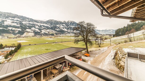 A view from a balcony overlooking a rural landscape with snow-covered mountains, a dirt path, and a wooden building with a metal roof. - Aberghof Apartments (Fuegen)