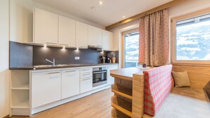 A modern kitchen with white cabinets, a wooden countertop, and a built-in oven. There is a window with curtains and a view of a snowy landscape. - Aberghof Apartments (Fuegen)
