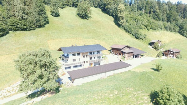 A multi-story building with a flat roof, surrounded by a grassy landscape and trees.