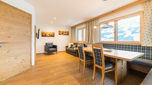 A modern kitchen with wooden flooring, a dining table with plaid chairs, a sofa, and a TV mounted on the wall. - Aberghof Apartments (Fuegen)