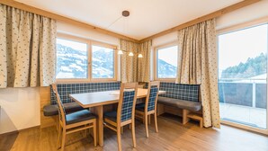 A dining area with a wooden table and chairs, a bench, and large windows with curtains. - Aberghof Apartments (Fuegen)