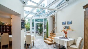 A bright, open-plan living area with a glass ceiling, a dining table, and a staircase leading to an outdoor area.