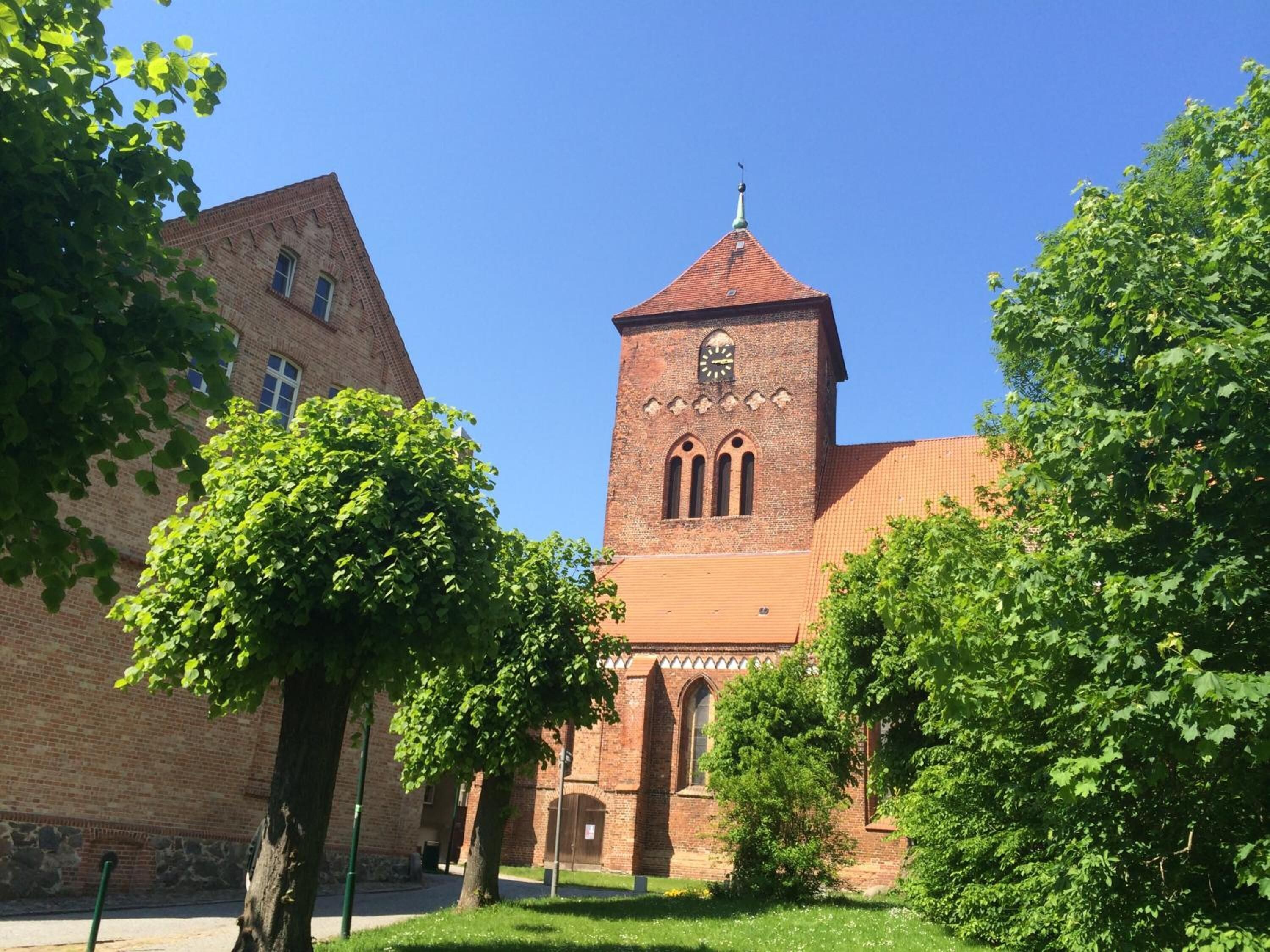 A brick building with a clock tower, surrounded by trees and a clear blue sky.