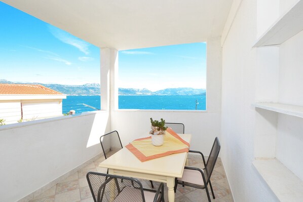 A balcony with a table and chairs, a potted plant, and a view of the sea and mountains.