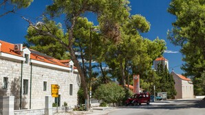 A building with a stone facade and a red-tiled roof, a street with a red car, and a sign indicating directions to Slatina and Trogir. - PETRA ARBANIJA - apt for 5+1 just few steps from the beach (Arbanija)