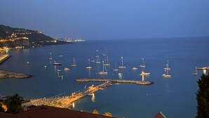 A coastal marina with numerous boats docked at piers, a small jetty, and a distant cityscape.