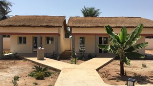 A building with two thatched-roof structures, a central pathway, and a banana tree in the foreground. - Séné-Marra haven of peace.  (Cap Skirring)