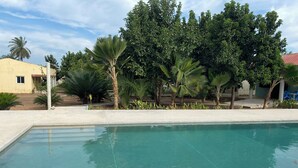 A swimming pool with clear water, surrounded by greenery and a building with a yellow facade. - Séné-Marra haven of peace.  (Cap Skirring)