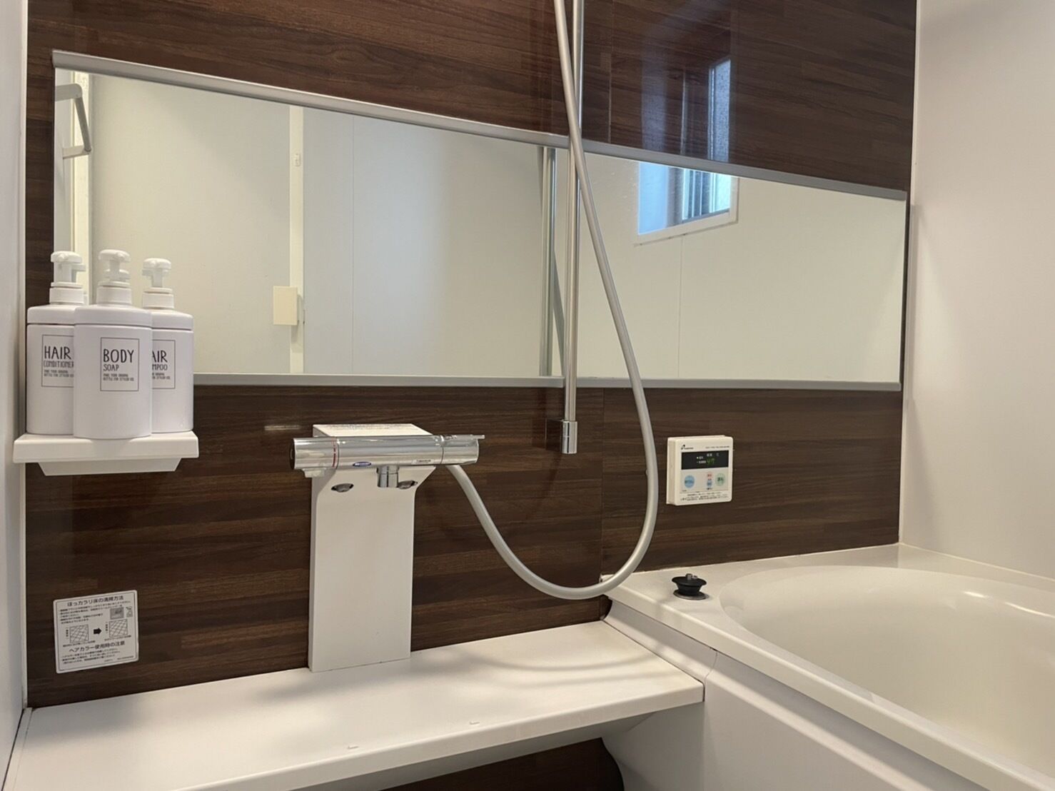 Un baño moderno con una bañera blanca, ducha con rociador manual y espejo sobre el lavabo.