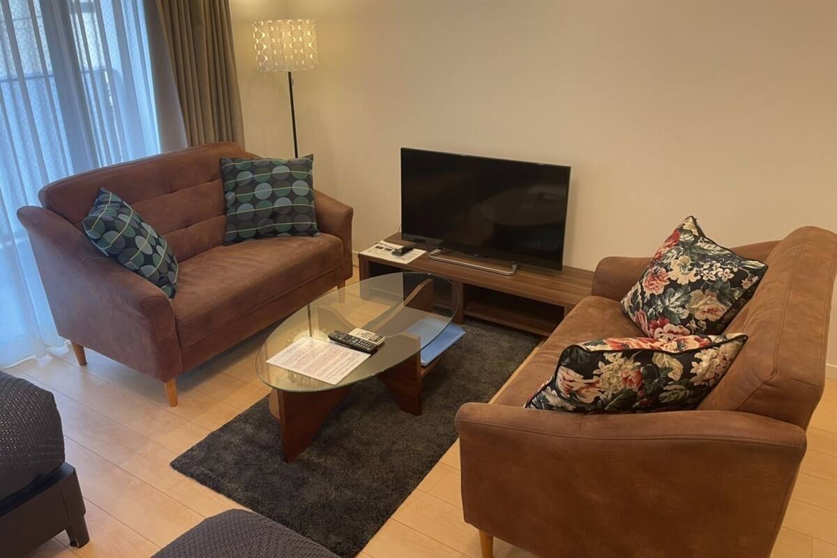 A living room with two brown sofas, a glass coffee table, a flat-screen TV, and a floor lamp.