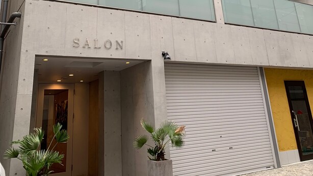 Een modern gebouw met een 'SALON' bord, grote ramen en een gesloten garage.