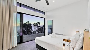 A modern bedroom with a large bed, a ceiling fan, and a view of trees through a sliding glass door. - Freycinet Coastal Retreat - Freycinet Holiday Houses (Coles Bay)